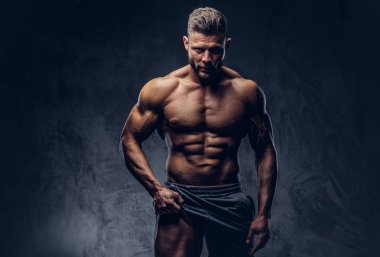 Şık saç ve sakal, bir yakışıklı gömleksiz dövmeli vücut geliştirmeci portresi kendine güvenen bir bakışla, bir stüdyoda ayakta kameraya bakarak onun bacaklarını kaslarının gösterir. Karanlık bir izole