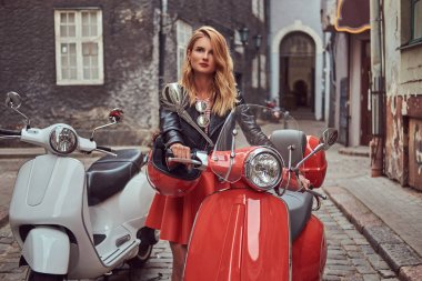 Şık kıyafetlerle iki retro scooter ile eski bir sokakta duran seksi sarışın kız.