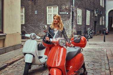 Şık kıyafetlerle iki retro scooter ile eski bir sokakta duran seksi sarışın kız.
