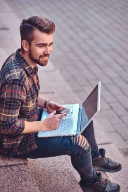 Basamaklarında oturan bir dizüstü bilgisayar üzerinde çalışan bir Polar gömlek ve pantolon giyen güzel gülümseyen freelance şık saç ve sakal,.