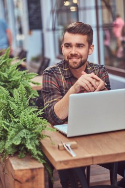 Şık saç ve sakal, gülümseyen genç freelance portresi giyinmiş bir kafe mekanlarda oturan bir dizüstü bilgisayar üzerinde çalışan bir Polar gömlek.