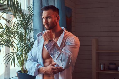 Yakışıklı kaslı kafkas erkek beyaz bir gömlek pencere sabah Giydir.