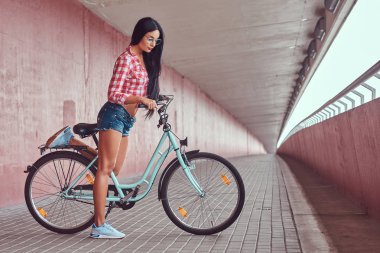 Pembe bir duvara şehir bisikleti ile poz pembe pazen tişört ve kot şort gözlük, bir seksi şık esmer kız.