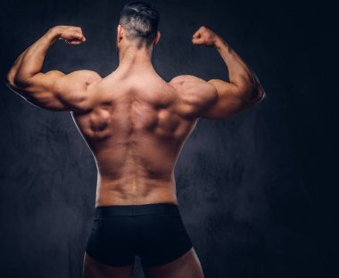 Arkadan görünüşü gömleksiz uzun boylu vücut geliştirmeci, bir stüdyo kaslarında gösterir. Karanlık bir arka plan üzerinde izole.