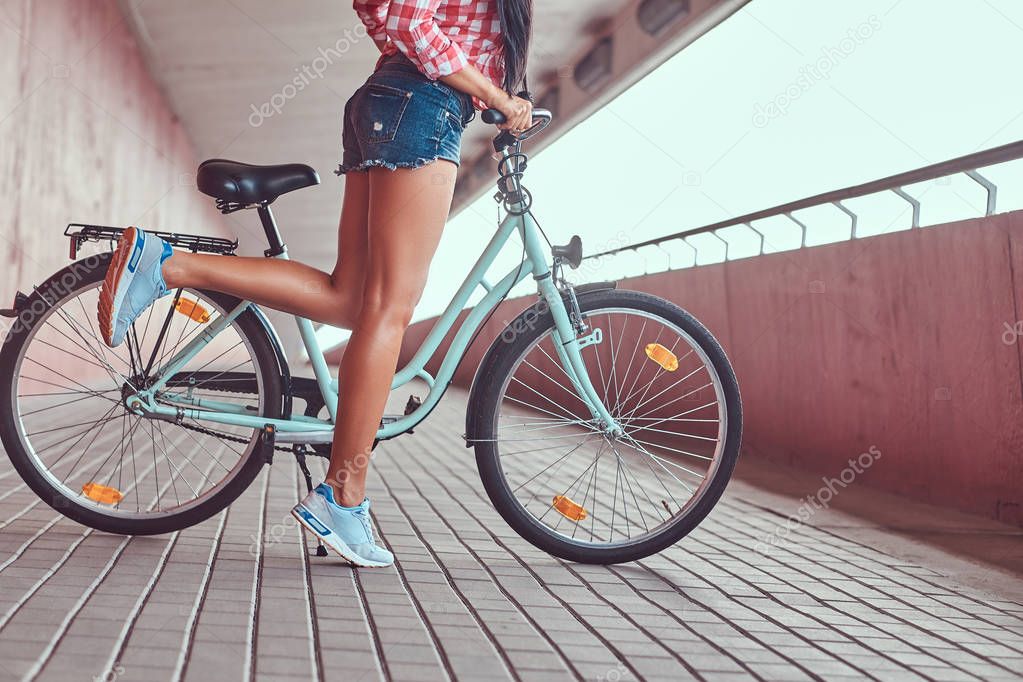 Close-up image of smooth slim female legs in a blue sneakers near the city bike.