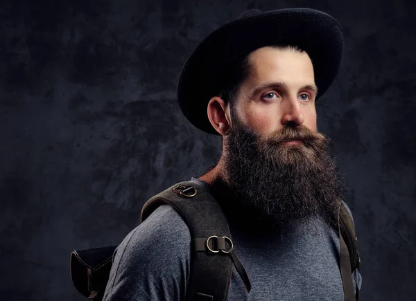 Yakın çekim yakışıklı bir portresi seyahat etmek sırt çantası ile şapkalı sakallı. Karanlık bir arka plan üzerinde izole.