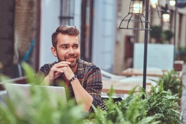 Şık saç ve sakal, gülümseyen genç freelance portresi giyinmiş bir kafe mekanlarda oturan bir dizüstü bilgisayar üzerinde çalışan bir Polar gömlek.