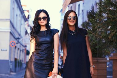 Şık siyah giyen iki seksi esmer içinde güneş gözlüğü elbise, bir teras kafe şehrin yakınında standları.