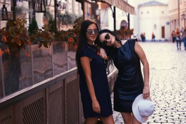 Şık siyah giyen iki seksi esmer içinde güneş gözlüğü elbise, bir teras kafe şehrin yakınında standları.