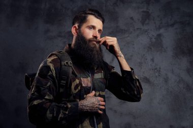 Yakışıklı bir gezgin, karanlık bir arka plan üzerinde izole bir stüdyoda ayakta bir tattoed kollu trendy Kamuflaj ceketi giymiş sakallı.
