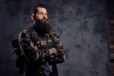 Yakışıklı bir gezgin, karanlık bir arka plan üzerinde izole bir stüdyoda ayakta bir tattoed kollu trendy Kamuflaj ceketi giymiş sakallı.