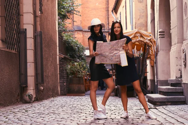 Due turisti donne sono in piedi in mezzo a una strada stretta, e cercare attrazioni sulla mappa . — Foto Stock