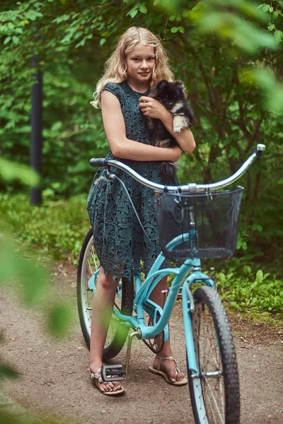 Porträtt av en liten blond flicka i en casual klänning, innehar söt spitz hund, i en park. — Stockfoto