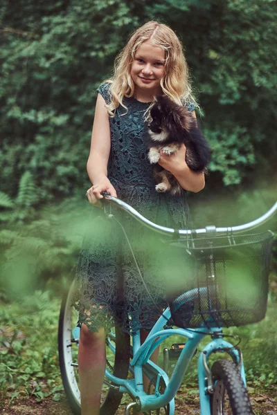 Ritratto di una bambina bionda in abito casual, tiene in braccio un simpatico cane spitz, in un parco . — Foto Stock