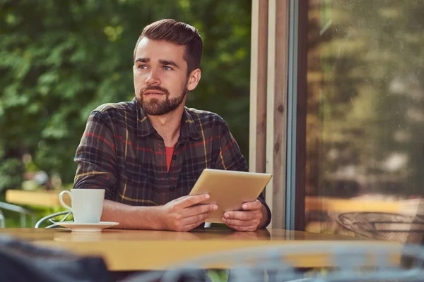 Een knappe modieuze mannelijke freelancer met stijlvolle kapsel en baard, het dragen van fleece shirt, werken op een tablet-pc in een café. — Stockfoto