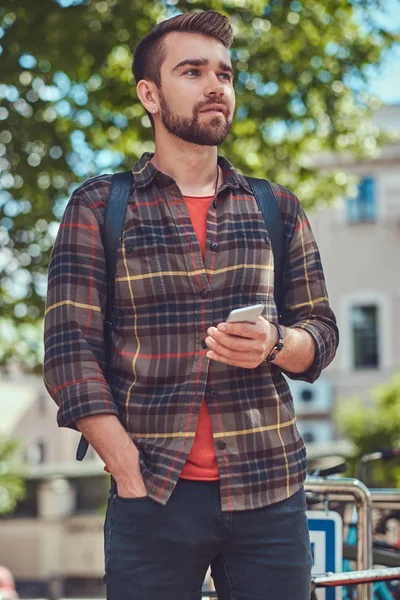 En stilig fashionabla unga hane med snygg frisyr och skägg, klädd i fleece tröja, står på parkeringen för cyklar i parken. — Stockfoto