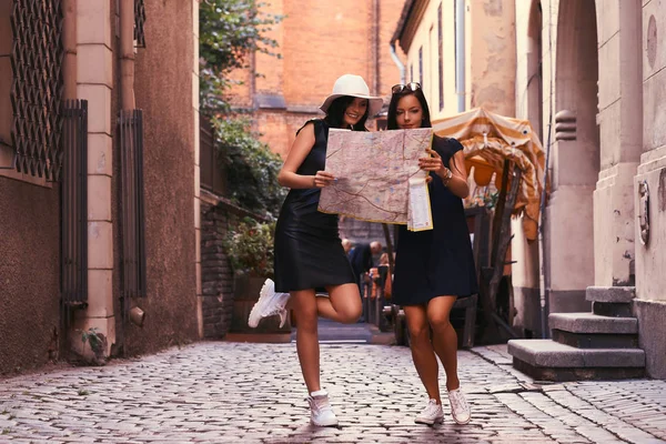 Két nő turisták közepén egy keskeny utcán, és keresse meg a látnivalók a térképen. — Stock Fotó