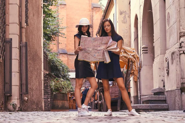 Deux touristes femmes sont debout au milieu d'une rue étroite, et chercher des sites sur la carte . — Photo