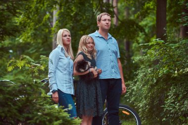 Çekici bir aile bir bisiklet yolculuğu ile parkta duran sevimli küçük spitz köpekleri, rahat kıyafetler giymiş.