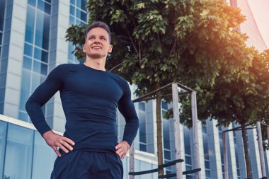 Modern kentin bir gökdelen karşı duran siyah bir spor giyim gülümseyen yakışıklı adam.