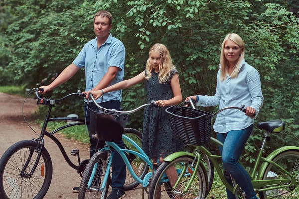 An attractive family dressed in casual clothes on a bicycle ride with their cute little spitz dog.