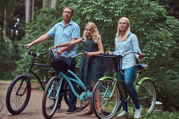An attractive family dressed in casual clothes on a bicycle ride with their cute little spitz dog.