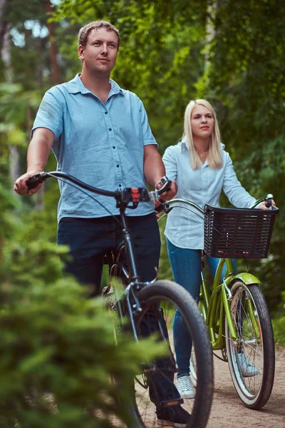 ブロンドの女性と男性の魅力的なカップルが公園で自転車に乗ってカジュアルな服を着た — ストック写真