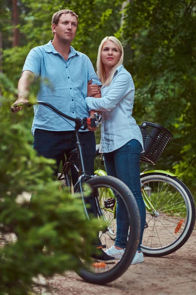 有吸引力的一对金发女郎和身着便装的男士 在公园附近的自行车上拥抱 — 图库照片
