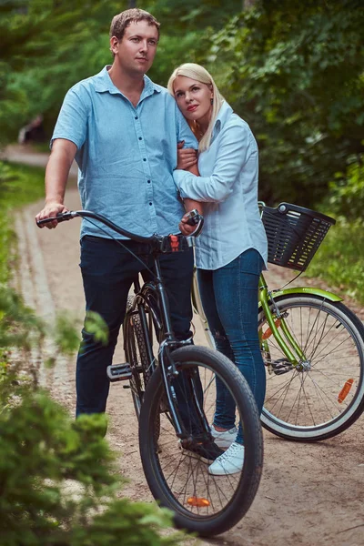 有吸引力的一对金发女郎和身着便装的男士 在公园附近的自行车上拥抱 — 图库照片