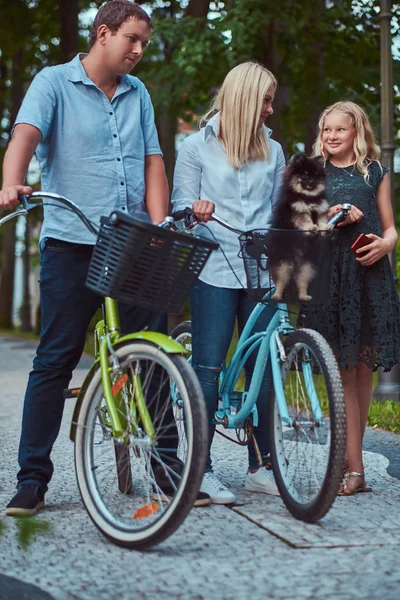 一个有吸引力的家庭穿着休闲衣服骑自行车与他们可爱的小斯皮茨狗 — 图库照片