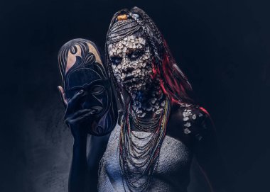 Taşlaşmış bir kırık Cilt ve dreadlocks, korkutucu Afrika şaman erkek portresi geleneksel maske karanlık bir arka plan üzerinde tutar. Kalıcı makyaj kavramı.