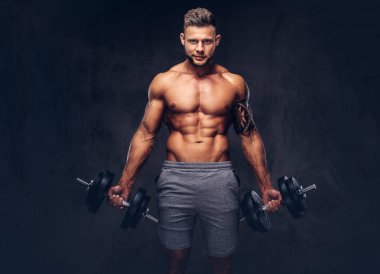 Bir stüdyoda poz spor şort giyen bir yakışıklı gömleksiz dövmeli vücut geliştirmeci şık saç ve sakal, ile. Karanlık bir arka plan üzerinde izole