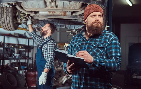 Dwóch brodatych brutalny mechanika naprawy samochodu na windę w garażu. — Zdjęcie stockowe