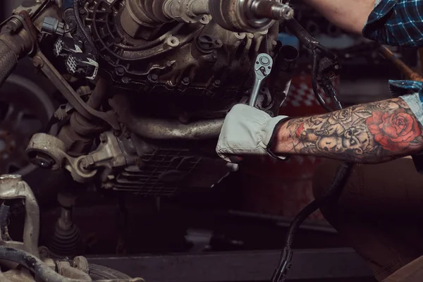 Imagen de cerca de un especialista mecánico tatuado repara el motor del coche con una llave inglesa en el garaje . —  Fotos de Stock