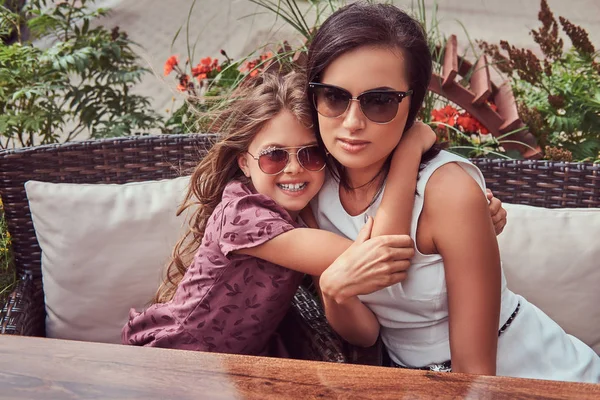 Retrato de la madre de moda y su encantadora hija durante un tiempo en un café al aire libre . — Foto de Stock