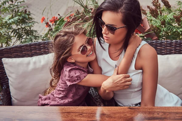 Retrato de la madre de moda y su encantadora hija durante un tiempo en un café al aire libre . — Foto de Stock