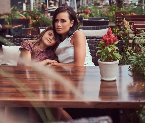 Retrato de la madre de moda y su encantadora hija durante un tiempo en un café al aire libre . — Foto de Stock