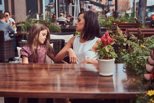 Portrait of fashionable mom and her lovely daughter during a time in an outdoor cafe.