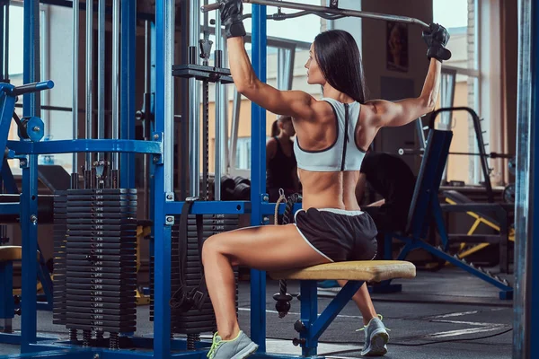 Mooie sexy atletische jonge brunette in een sportkleding trainen, trainen oppompen van terug lats spieren in de sportschool. — Stockfoto