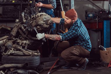 Acımasız dövmeli sakallı mekanik uzman Hidrolik Asansör garaja kaldırdı arabanın motoru onarır. Servis istasyonu.