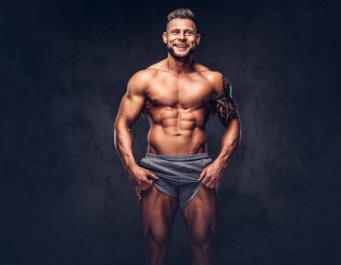 Bir stüdyoda poz spor şort giyen bir yakışıklı gömleksiz dövmeli vücut geliştirmeci şık saç ve sakal, ile. Karanlık bir arka plan üzerinde izole