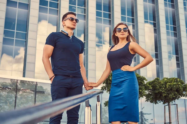 Atractiva pareja de moda, sexy chica rubia y hombre guapo de pie en la ciudad moderna contra un rascacielos . — Foto de Stock