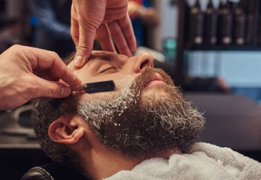 Kuaför sakalını tehlikeli bir ustura ile tıraş ederken erkek Kuaför Salonu bir koltukta otururken yakışıklı bir hipster sakallı.