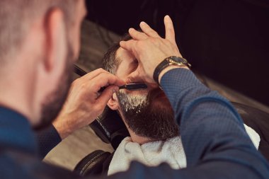 Kuaför sakalını tehlikeli bir ustura ile tıraş ederken erkek Kuaför Salonu bir koltukta otururken yakışıklı bir hipster sakallı.