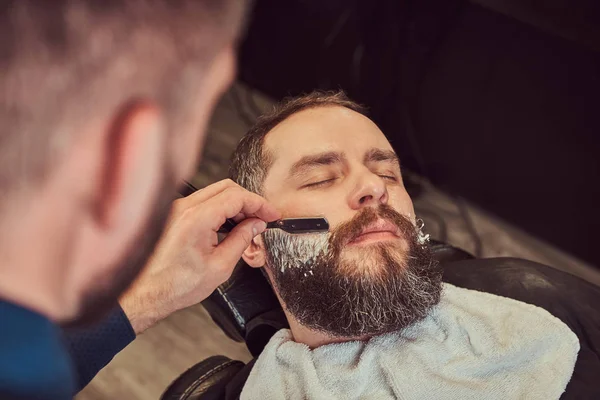 Kuaför sakalını tehlikeli bir ustura ile tıraş ederken erkek Kuaför Salonu bir koltukta oturan sakallı. — Stok fotoğraf