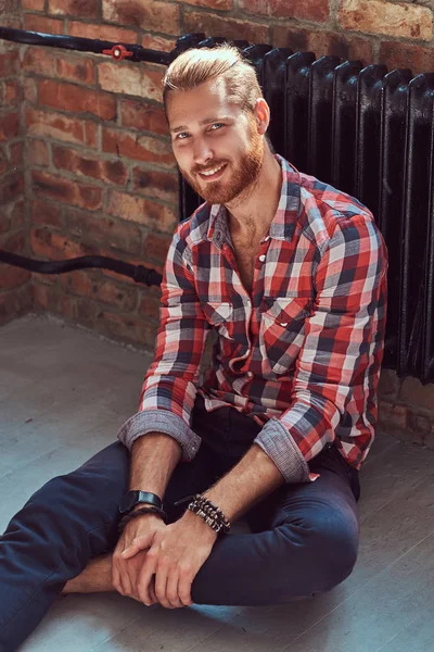 Joven guapo pelirroja modelo hombre se sienta en un piso en la habitación con un loft interior . —  Fotos de Stock