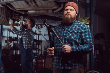 İki sakallı acımasız mekanik bir asansör garaja bir araba tamir. 