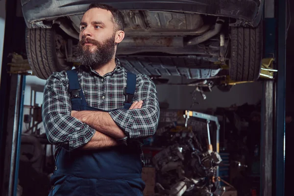 Two bearded brutal mechanics repair a car on a lift in the garage.