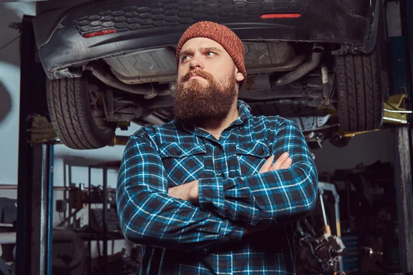 Two bearded brutal mechanics repair a car on a lift in the garage.