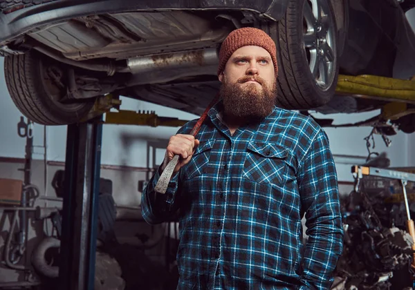 Two bearded brutal mechanics repair a car on a lift in the garage.